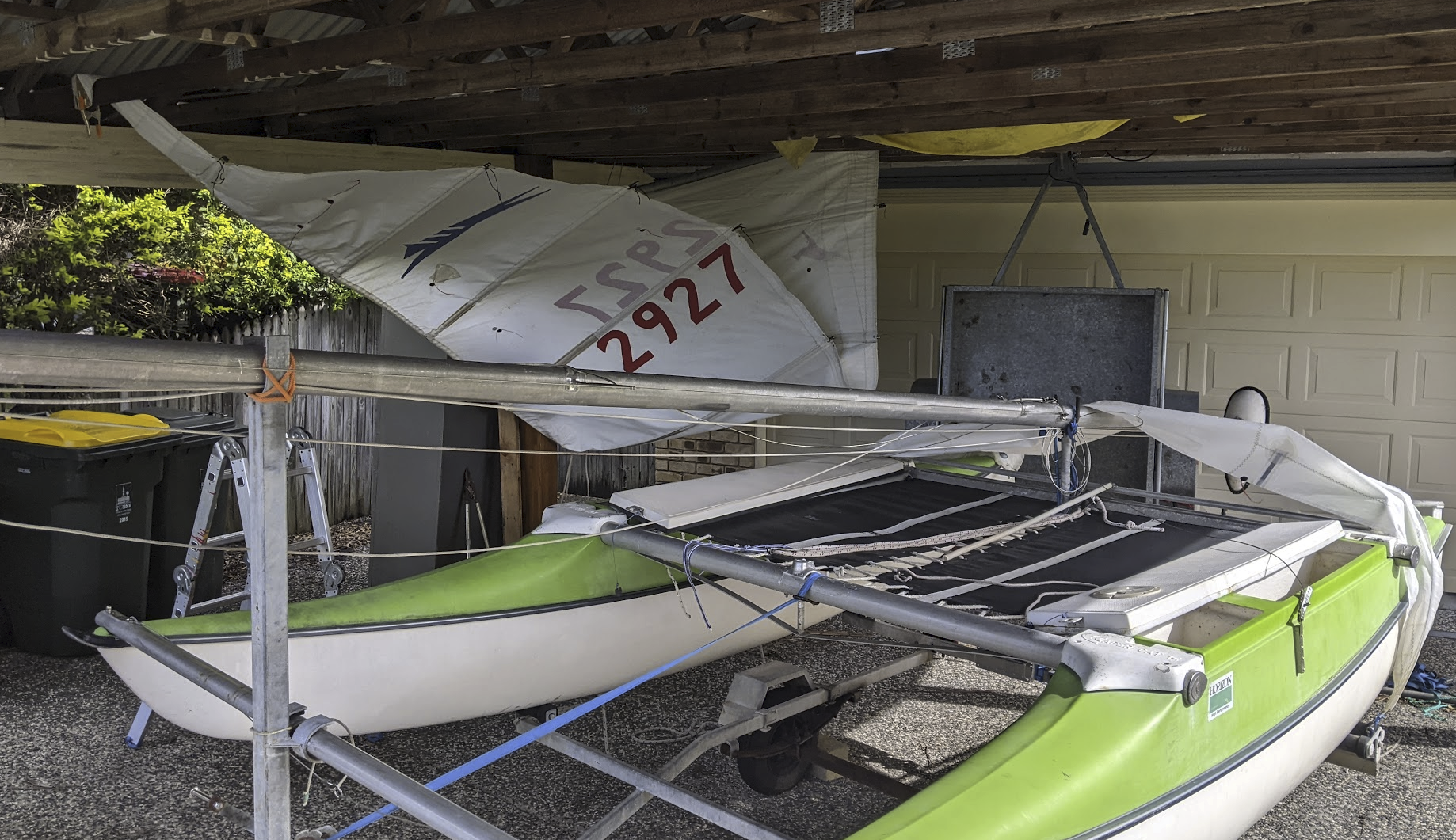 A photo of the boat under our carport with one sail hanging from the rafters and the other draped over the boat. A photo of the boat under our carport with one sail hanging from the rafters and the other draped over the boat.