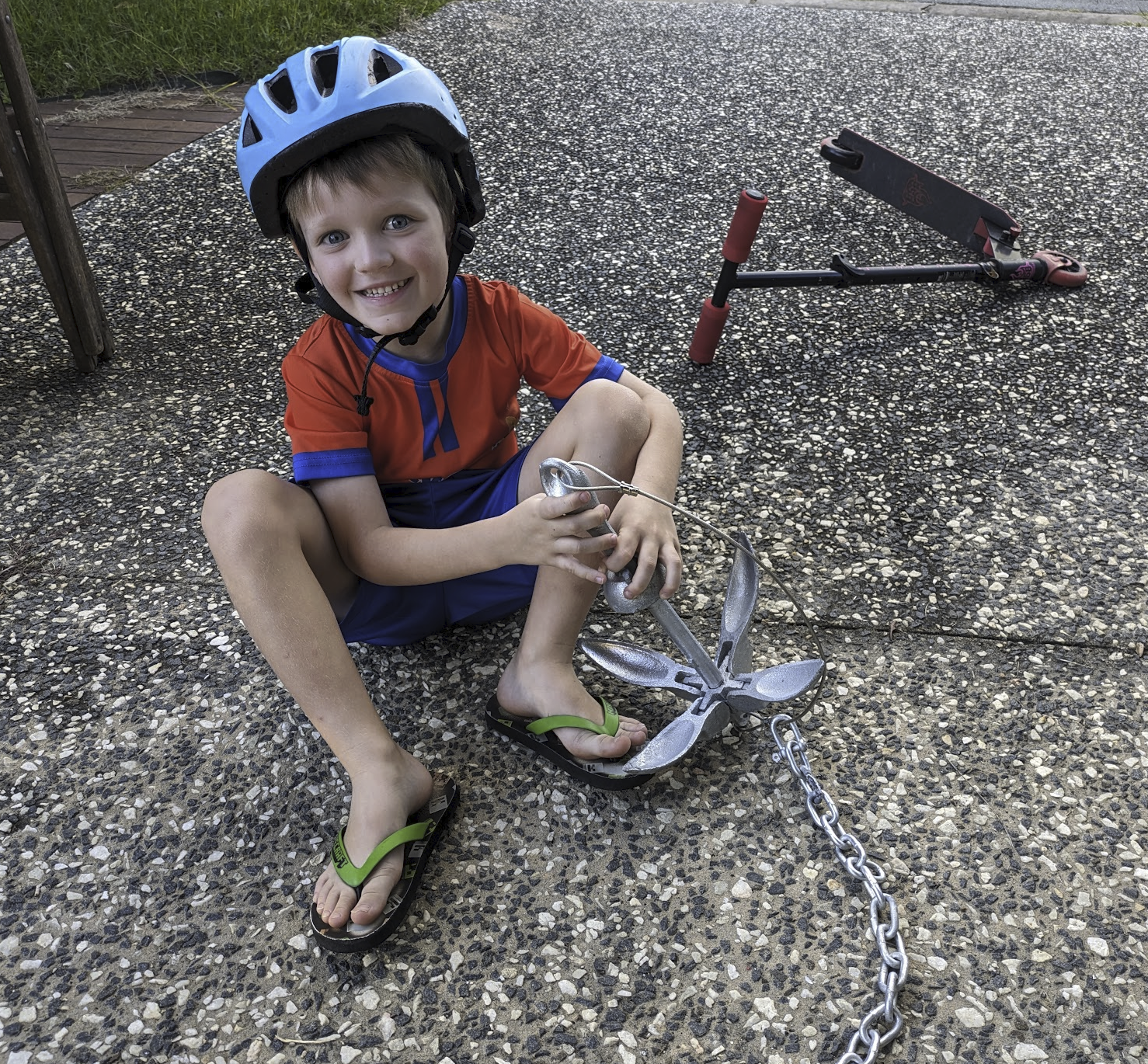 A photo of Sam, wearing a helmet, sitting on the driveway playing with a small anchor. A photo of Sam, wearing a helmet, sitting on the driveway playing with a small anchor.