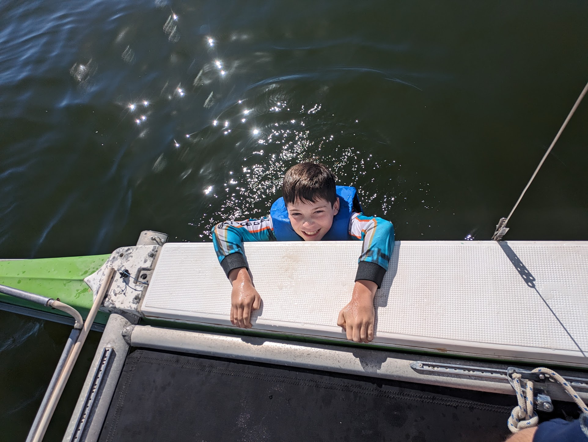 A photo of Alex smiling in the water, holding onto the boat. A photo of Alex smiling in the water, holding onto the boat.