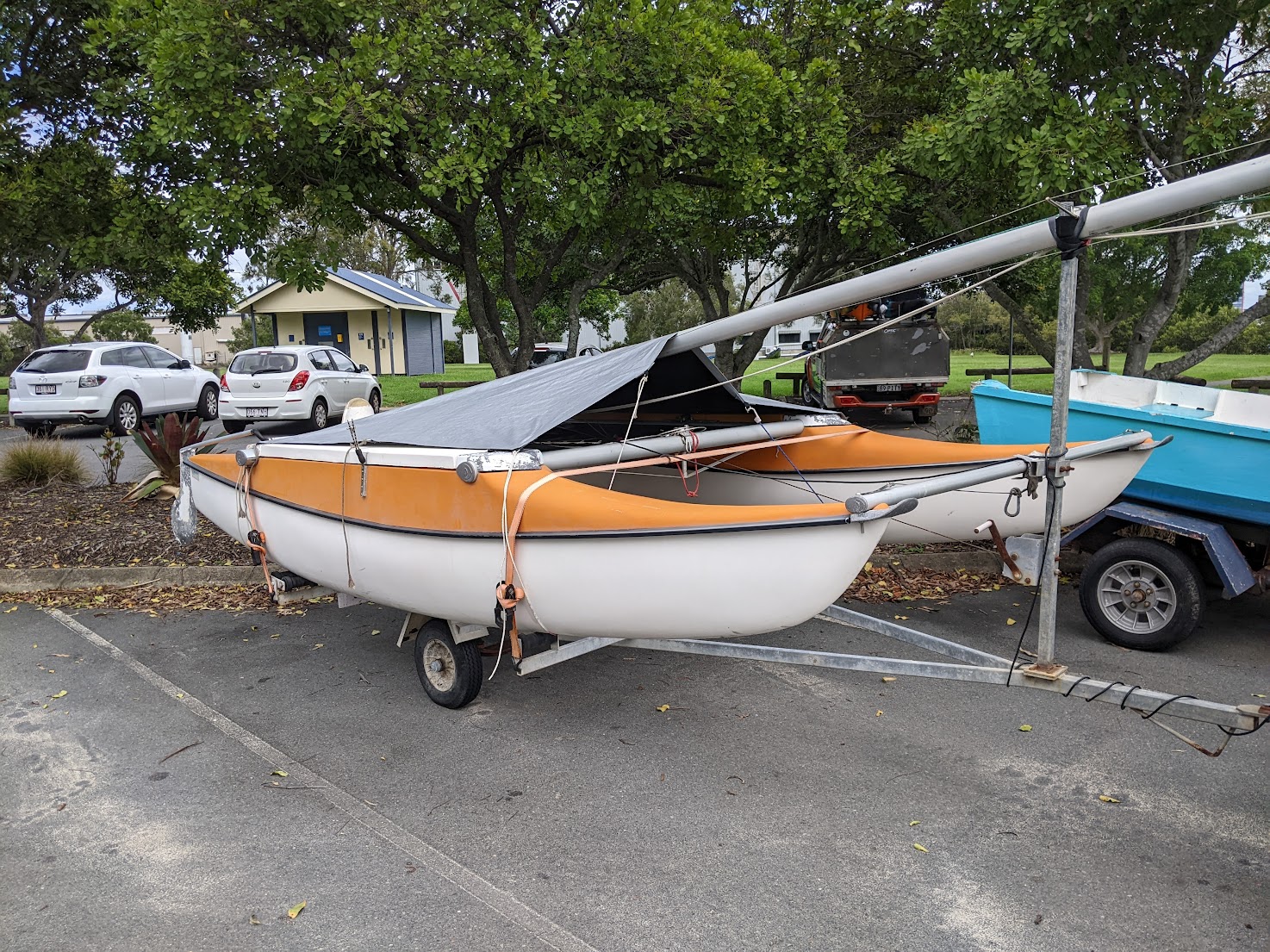 An orange and white caper cat with a tarp over it on a trailer in a parking lot. An orange and white caper cat with a tarp over it on a trailer in a parking lot.