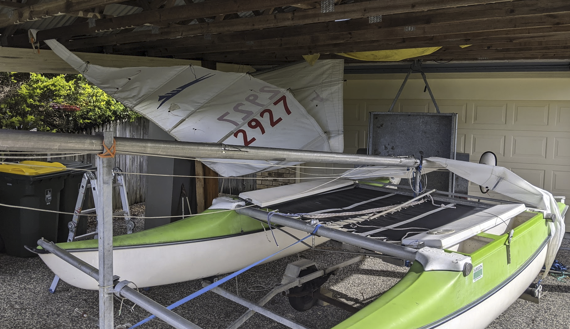 A photo of the boat under our carport with one sail hanging from the rafters and the other draped over the boat.