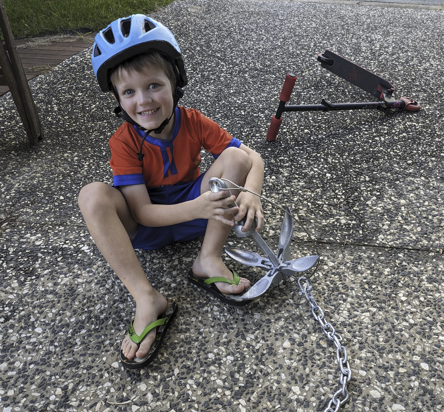 A photo of Sam, wearing a helmet, sitting on the driveway playing with a small anchor.