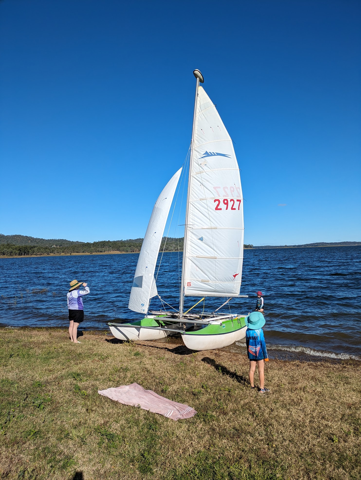 A photo of the boat pulled up onto some grass. Alex is standing in the water. Michelle and Sam are watching from the shore.