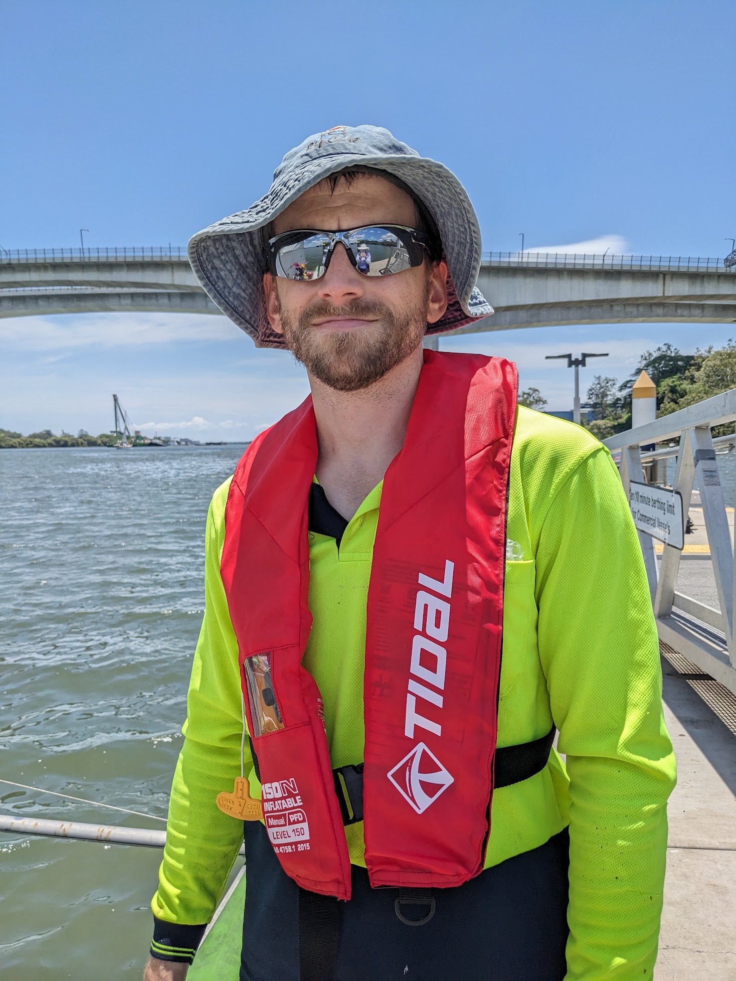 A photo of me, a man with a beard and a hat. A large concrete bridge is in the background.