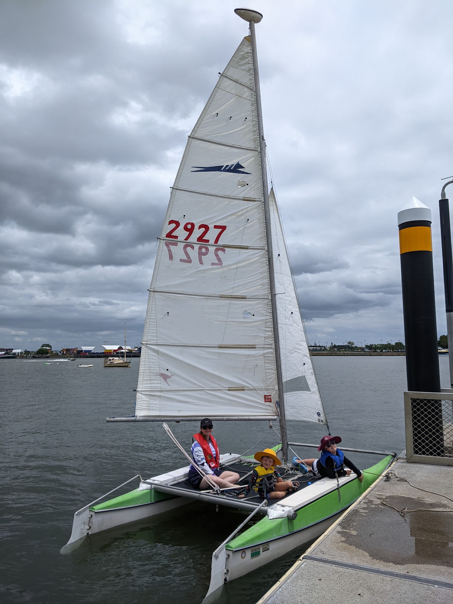 A photo of the boat on the water with sails up. The sky is overcast.