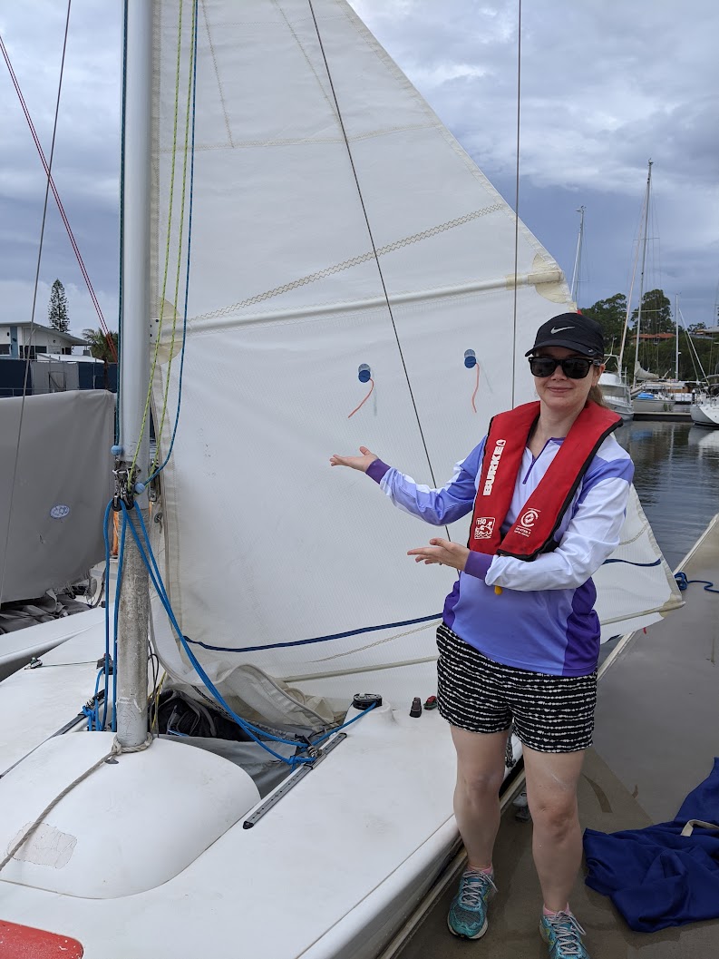 My wife standing next to an Elliot 6 at dock with a half-raised mainsail.