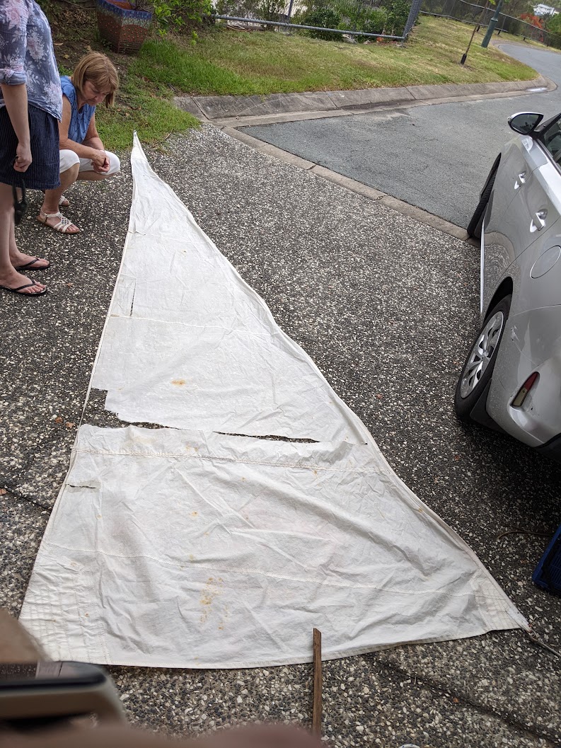 A photo of our old jib laying on the driveway. It is a triangle of sailcloth with a large rip across the middle.