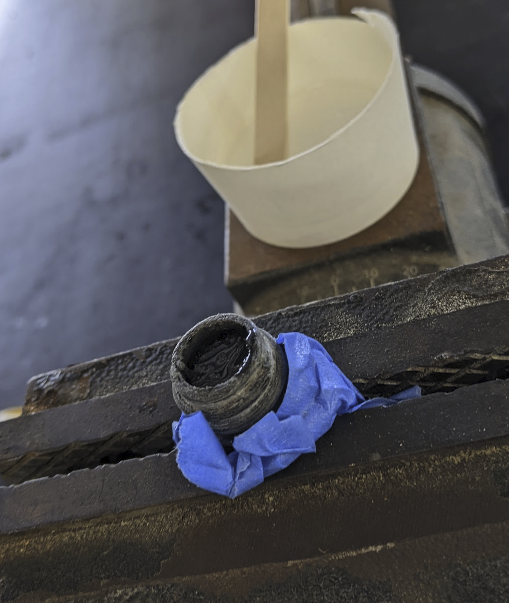 A photo of the bung wrapped in tape held in a vice filled with transparent epoxy.